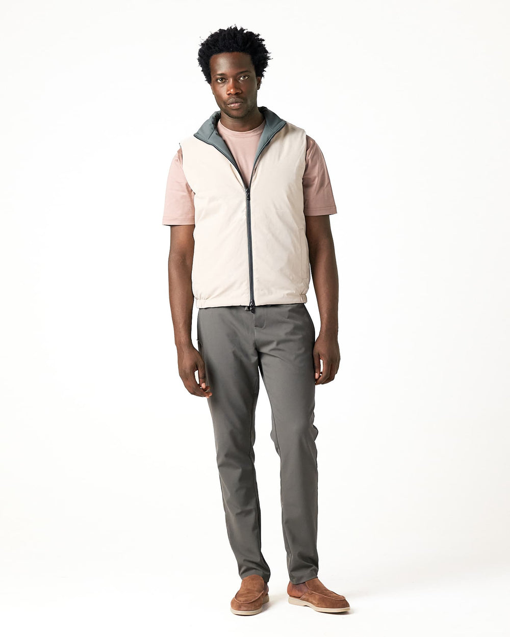 Man wearing a beige vest, pink shirt, gray pants, and brown shoes on a white background
