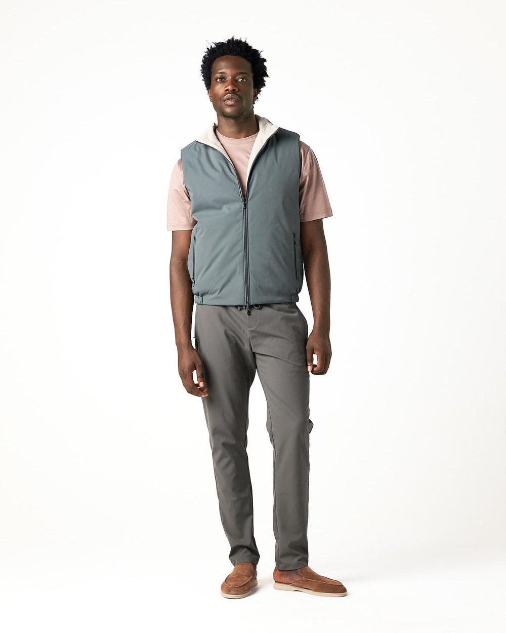 Man wearing a gray vest over a pink shirt with gray pants on a white background