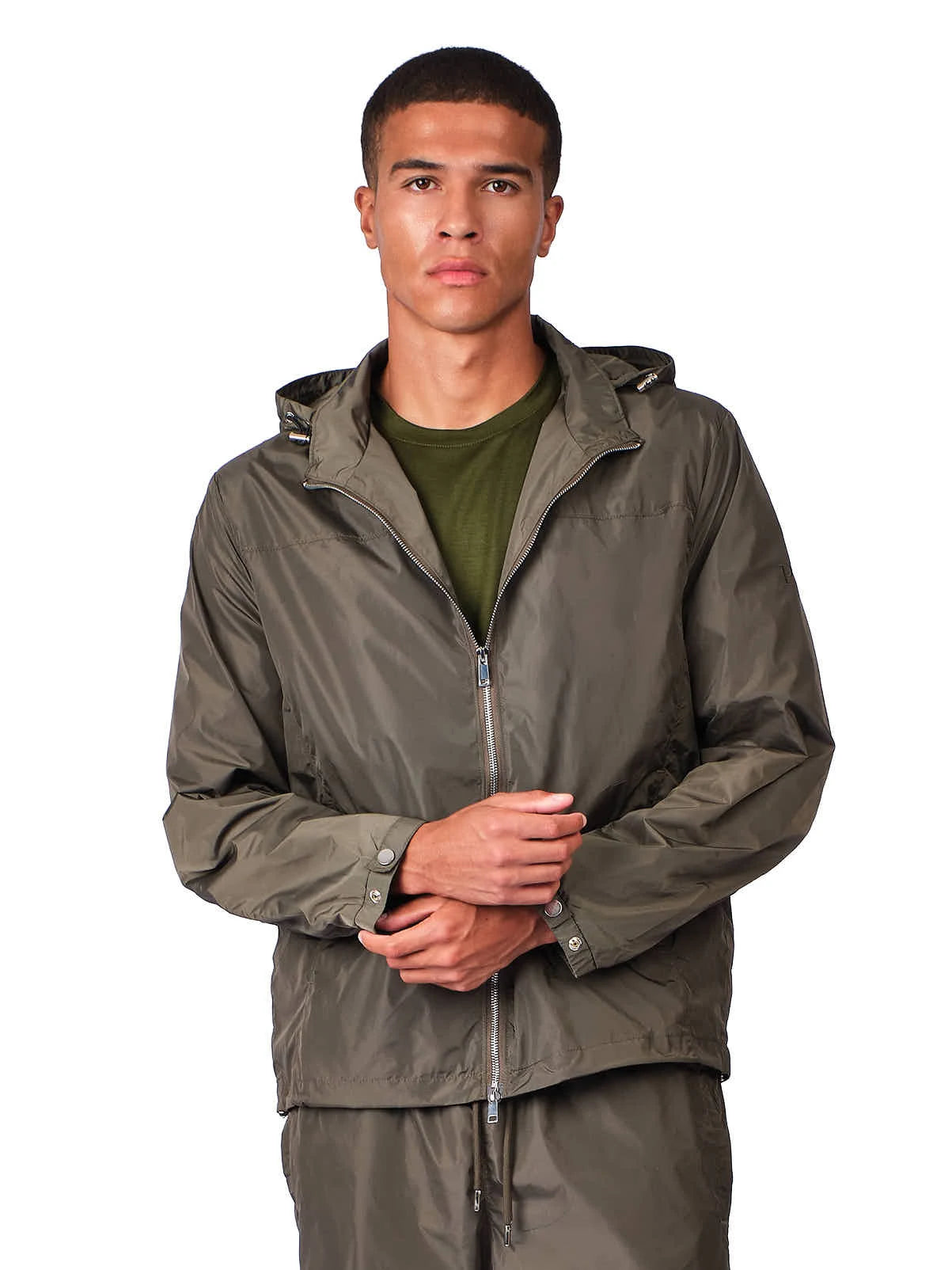 A man wearing an olive green hooded zip-up jacket over an olive green t-shirt, standing against a solid white background.