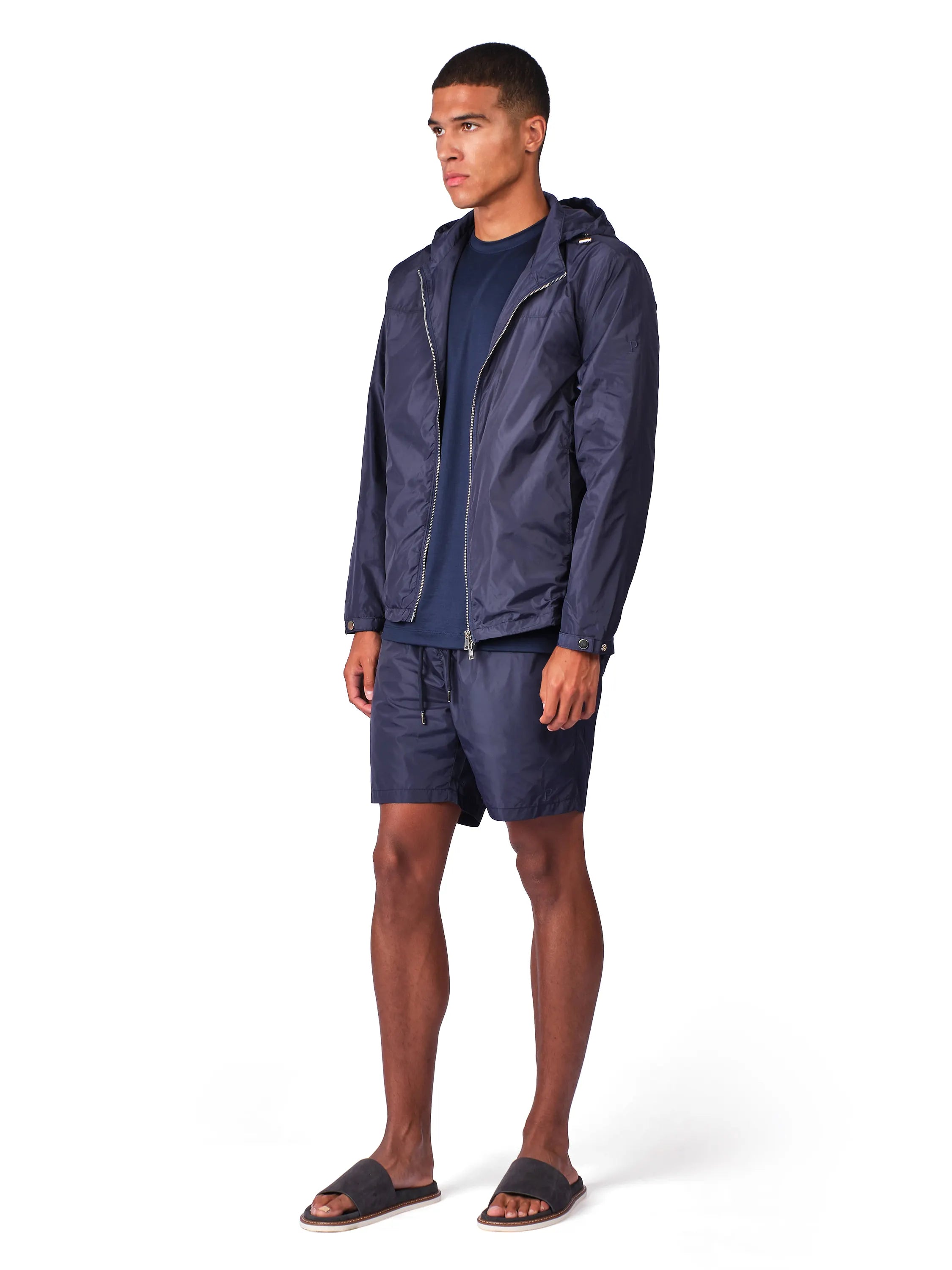 A man modeling a navy blue hooded jacket over a matching navy blue t-shirt and shorts, standing against a plain white background.