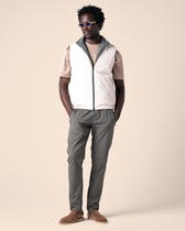 Man wearing a white vest over a beige shirt with gray pants on a beige background