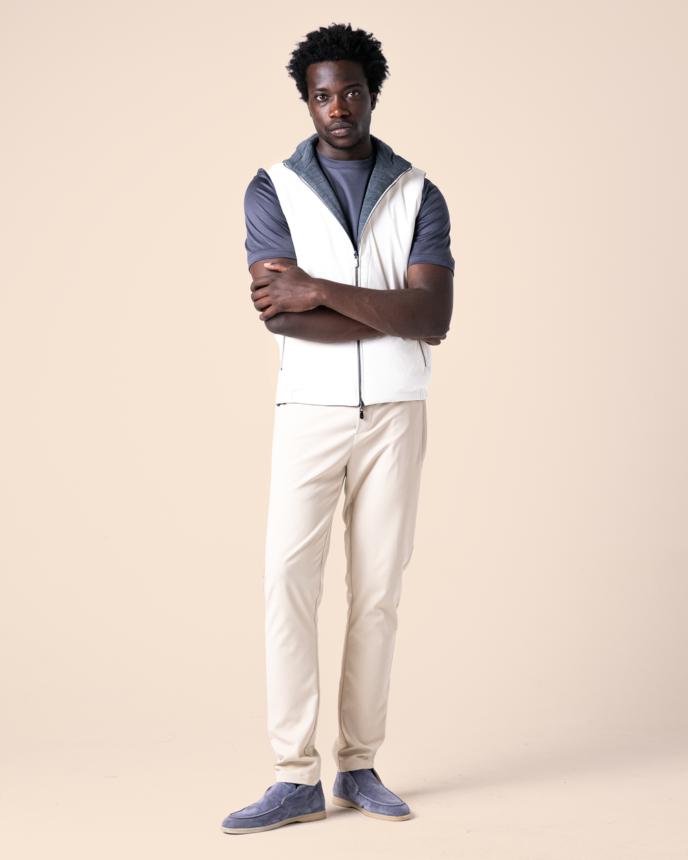 Man wearing a white vest over a blue shirt with beige pants on a beige background