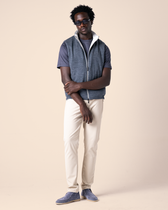 Man wearing a blue vest over a gray shirt, white pants, and blue shoes on a beige background