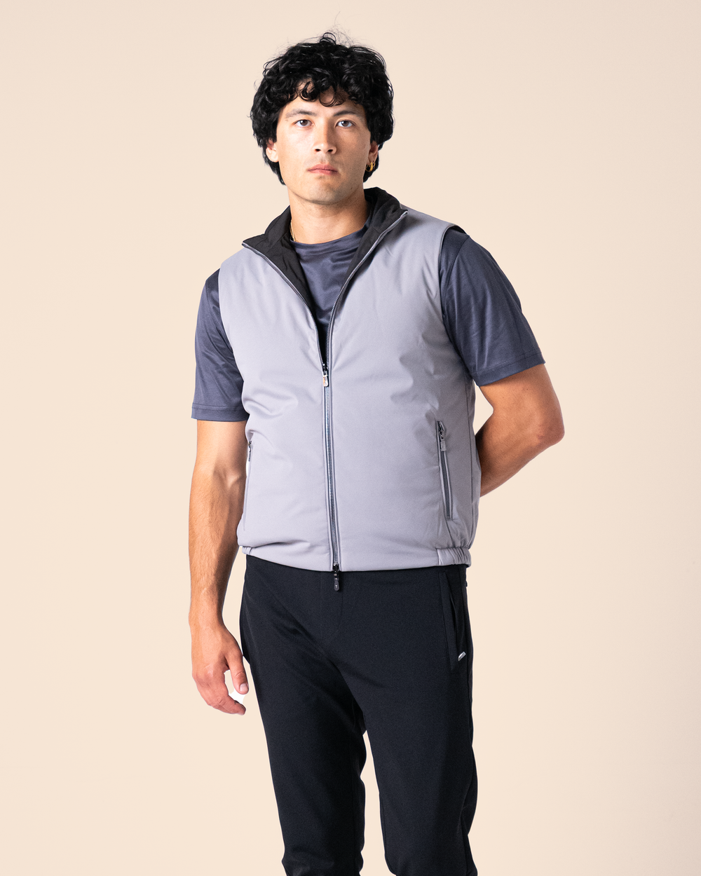 Man wearing a gray vest over a blue shirt with black pants on a beige background