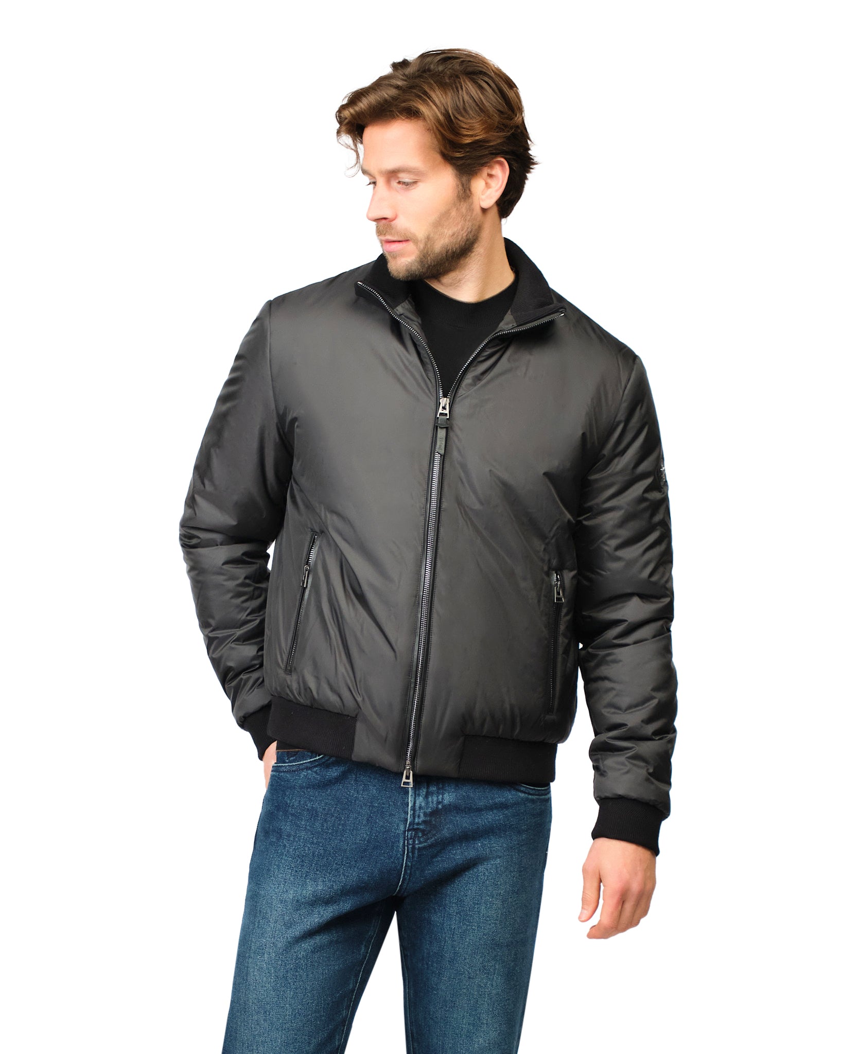 Man wearing a dark gray bomber jacket and blue jeans on a white background