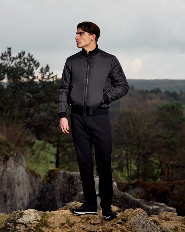Man in a black outfit standing on a rocky outcrop with a forest background