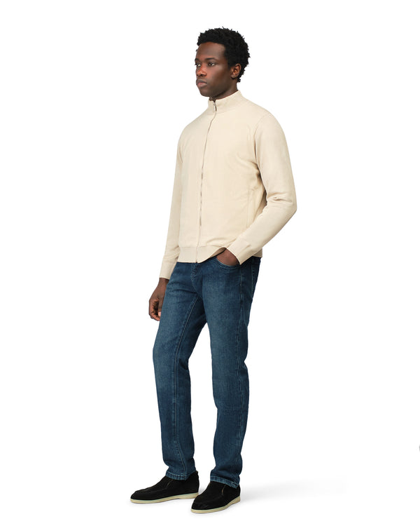 Man wearing a beige sweater and blue jeans on a white background