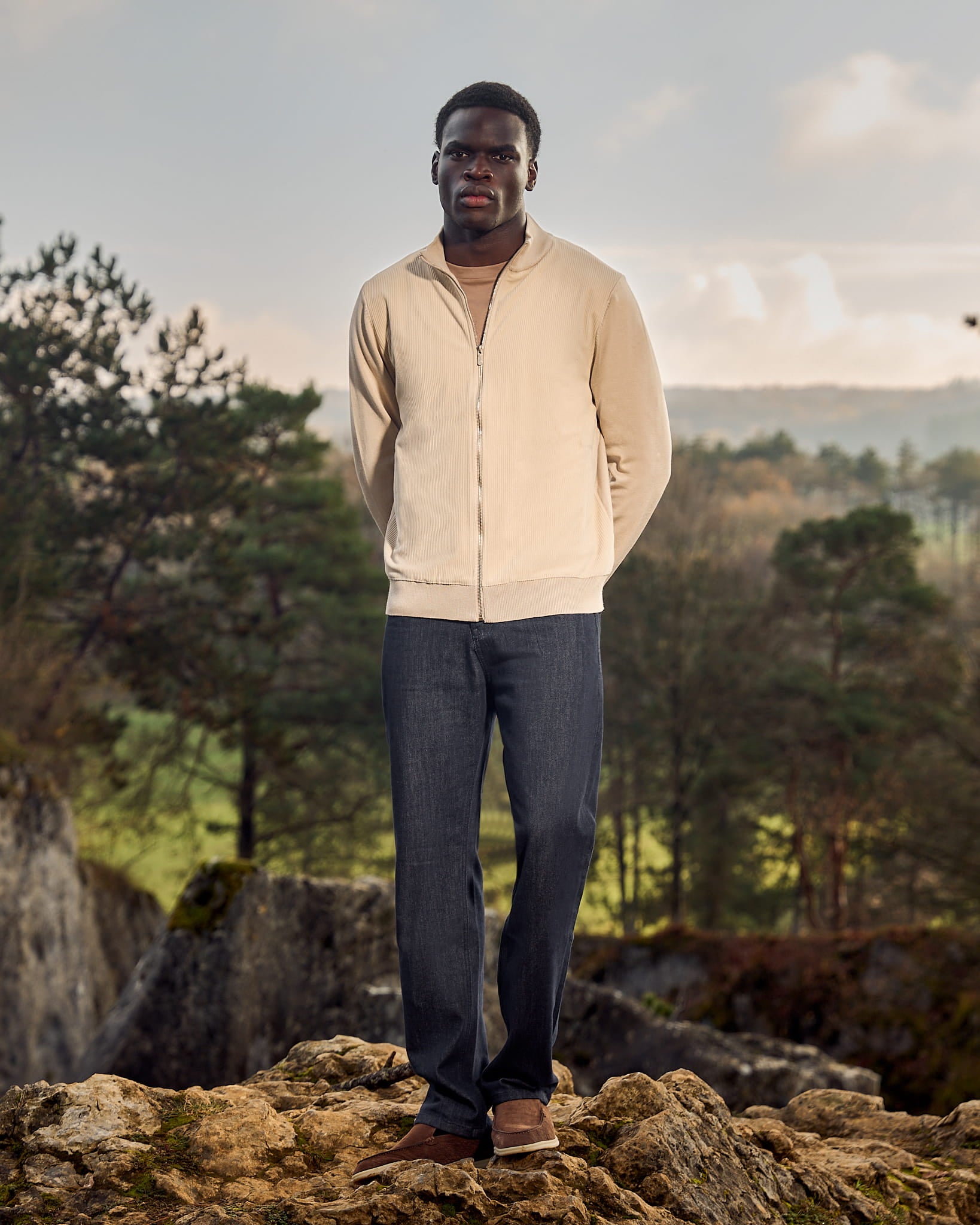 Man standing on a rocky outcrop with a scenic background of trees and mountains.