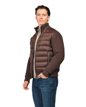 Man wearing a brown puffer vest over a sweater and jeans on a white background