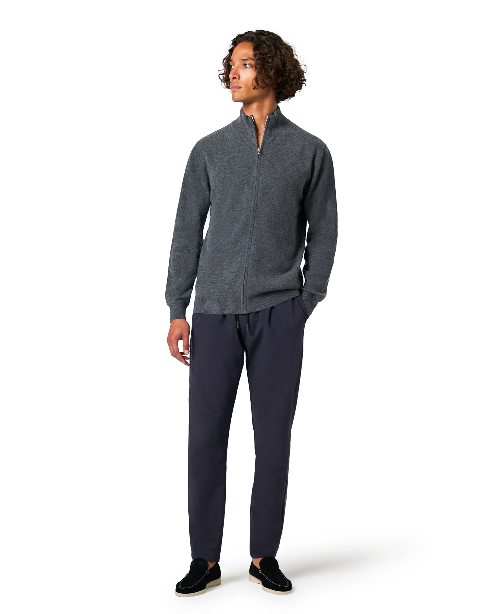 Man wearing a gray zip-up sweater and dark pants on a white background