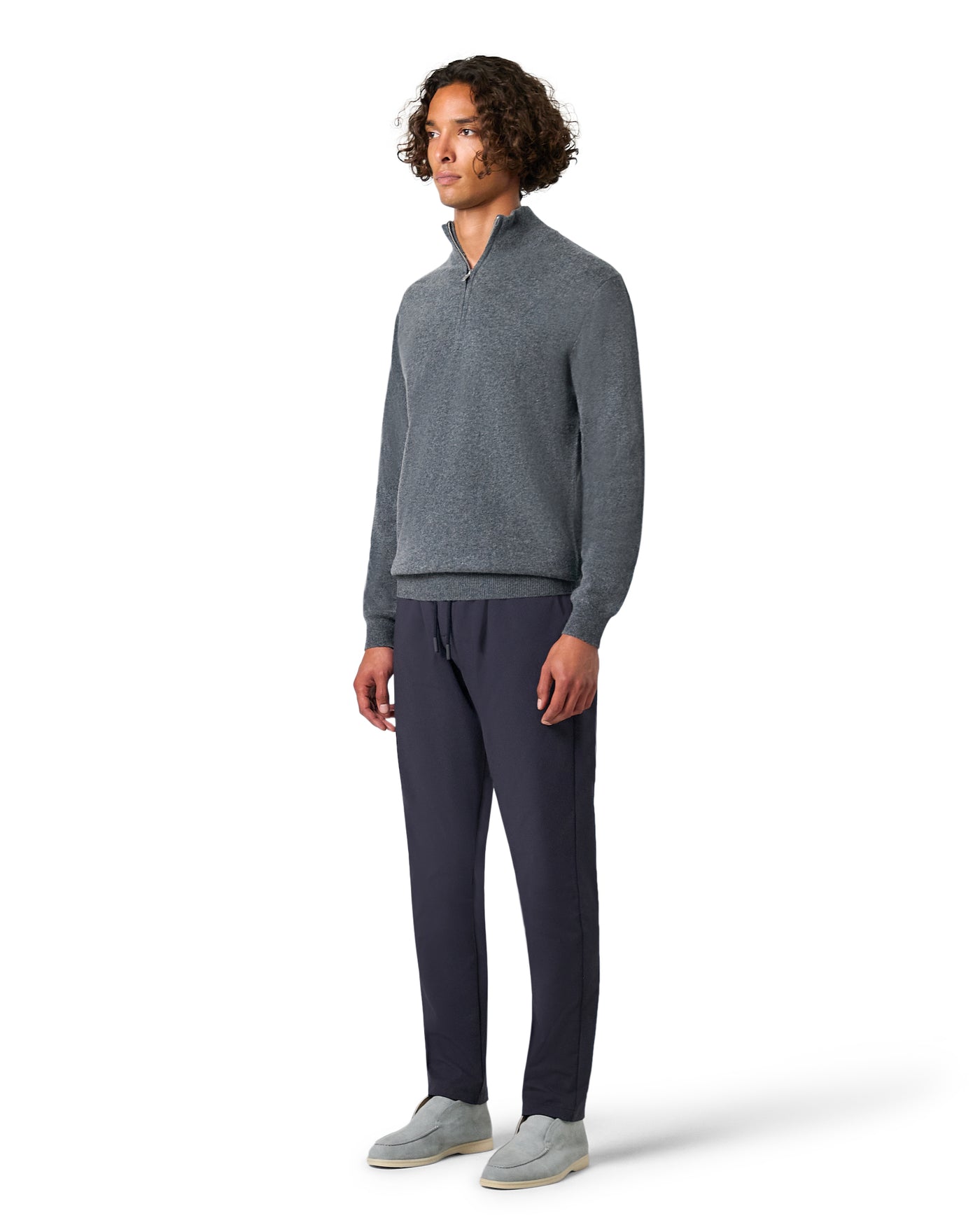 Man wearing a gray sweater and dark pants on a white background