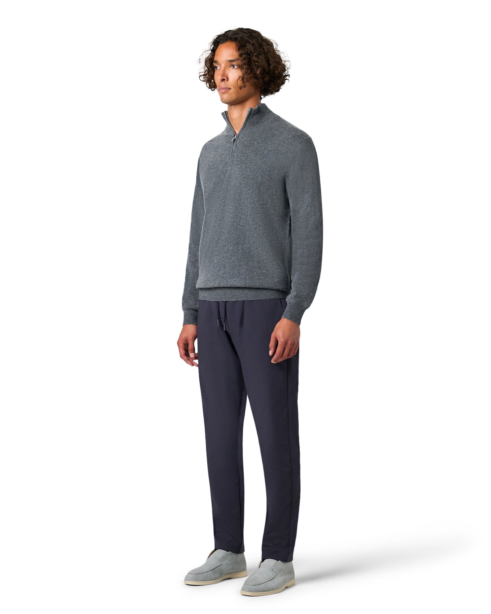 Man wearing a gray sweater and dark pants on a white background
