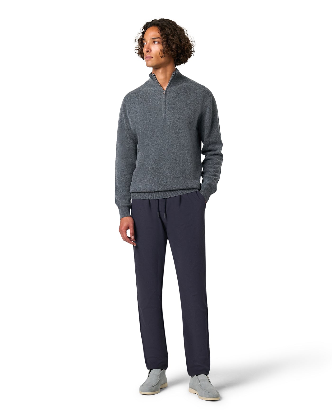 Man wearing a gray sweater and navy pants on a white background