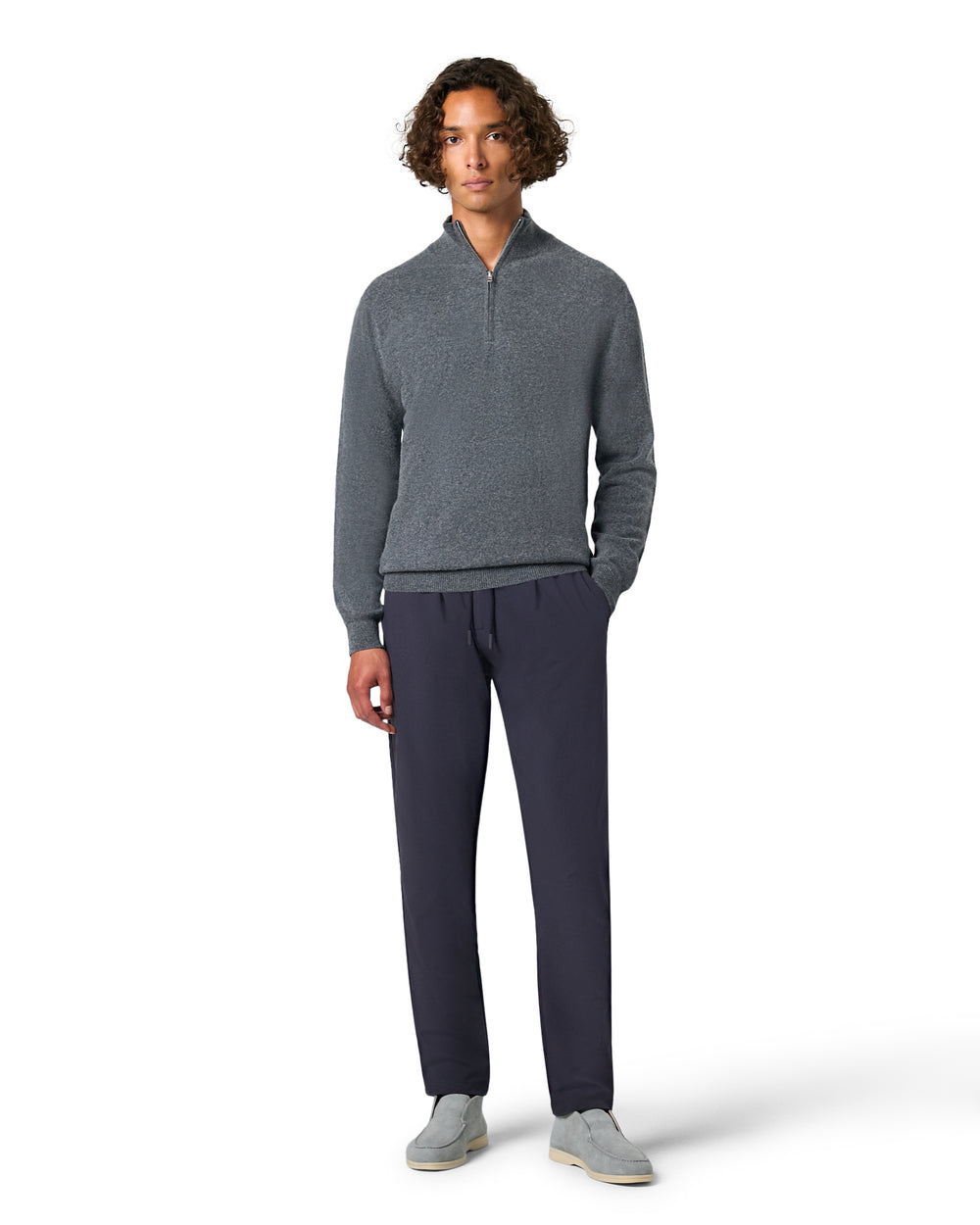 Man wearing a gray sweater and dark pants on a white background