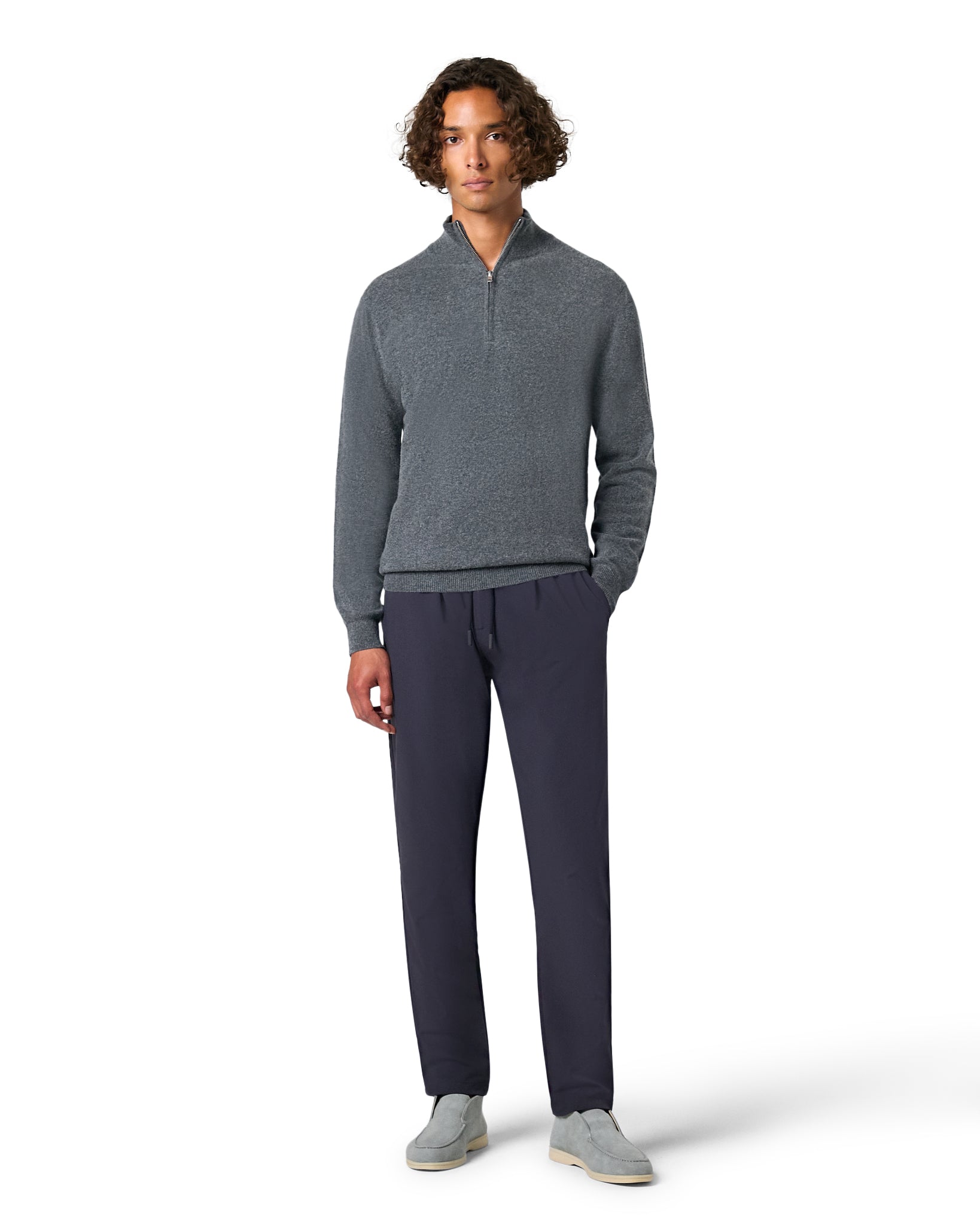 Man wearing a gray sweater and dark pants on a white background