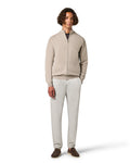 Man wearing a beige zip-up sweater and white pants on a white background