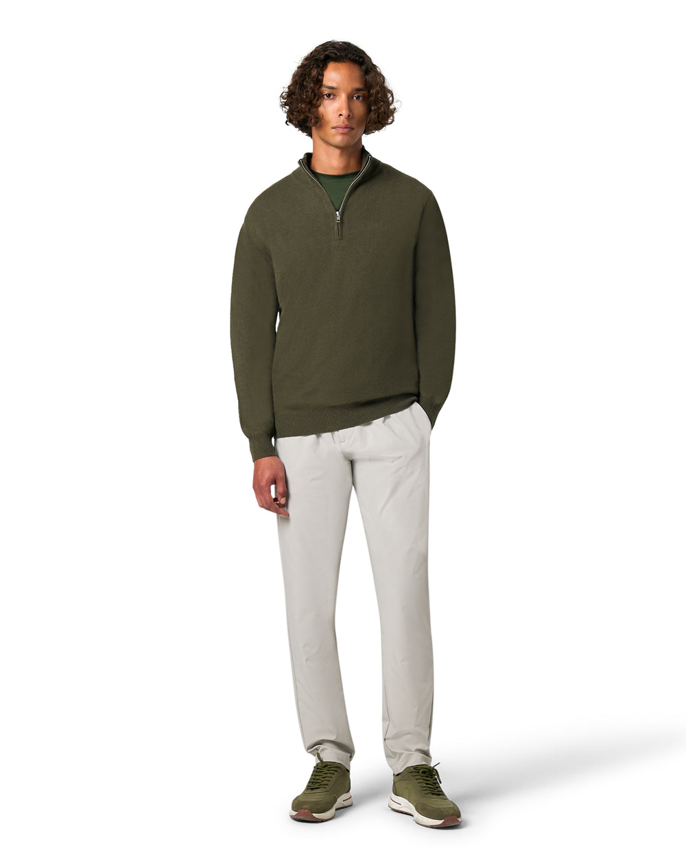 Man wearing a green pullover and light gray pants on a white background