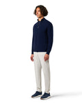 Man wearing a navy sweater and white pants on a white background