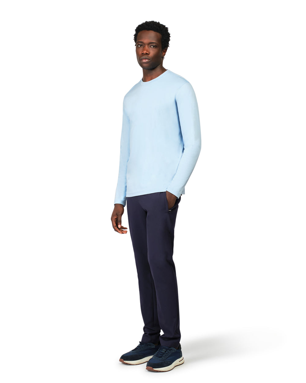Man wearing a light blue sweater and dark pants on a white background
