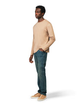Man wearing a beige sweater and blue jeans on a white background