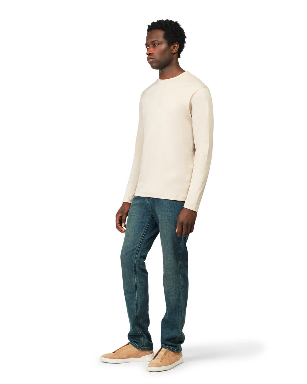 Man wearing a cream sweater and blue jeans on a white background