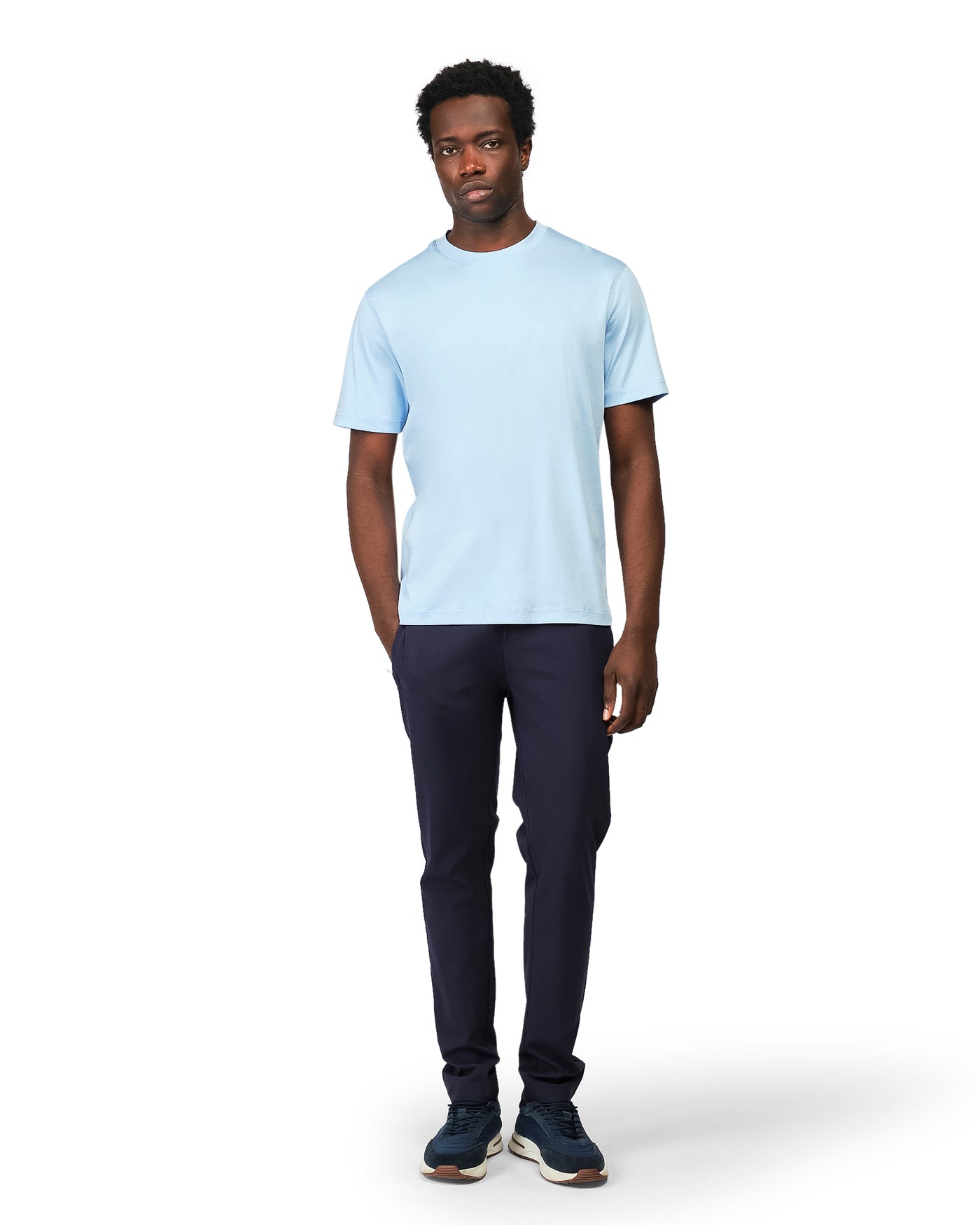 Man wearing a light blue t-shirt and dark pants on a white background