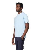 Man wearing a light blue t-shirt and dark pants on a white background