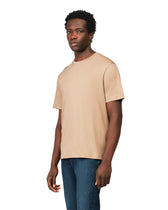 Man wearing a beige t-shirt and blue jeans on a white background