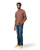 Man wearing a brown t-shirt and blue jeans on a white background