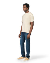 Man wearing a beige t-shirt and blue jeans on a white background