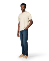 Man wearing a beige t-shirt and blue jeans on a white background