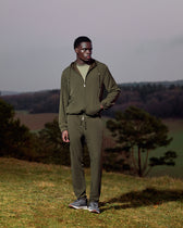 Man wearing a green tracksuit standing in a field with trees and a gray sky in the background
