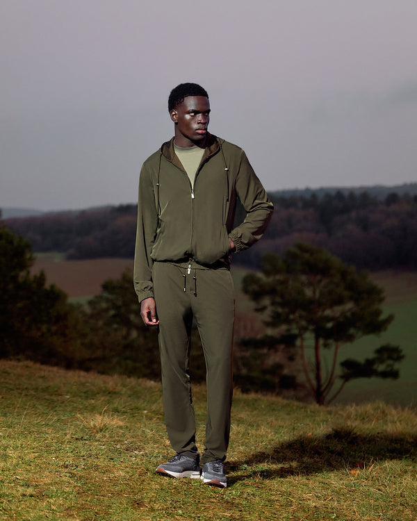 Man wearing a green tracksuit standing in a field with trees and a gray sky in the background
