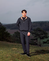 Man wearing a dark jacket and pants standing in a natural setting with trees and grass.