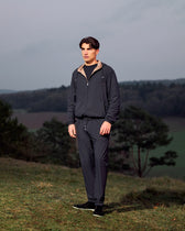 Man wearing a dark outfit standing on a grassy hill with a scenic background
