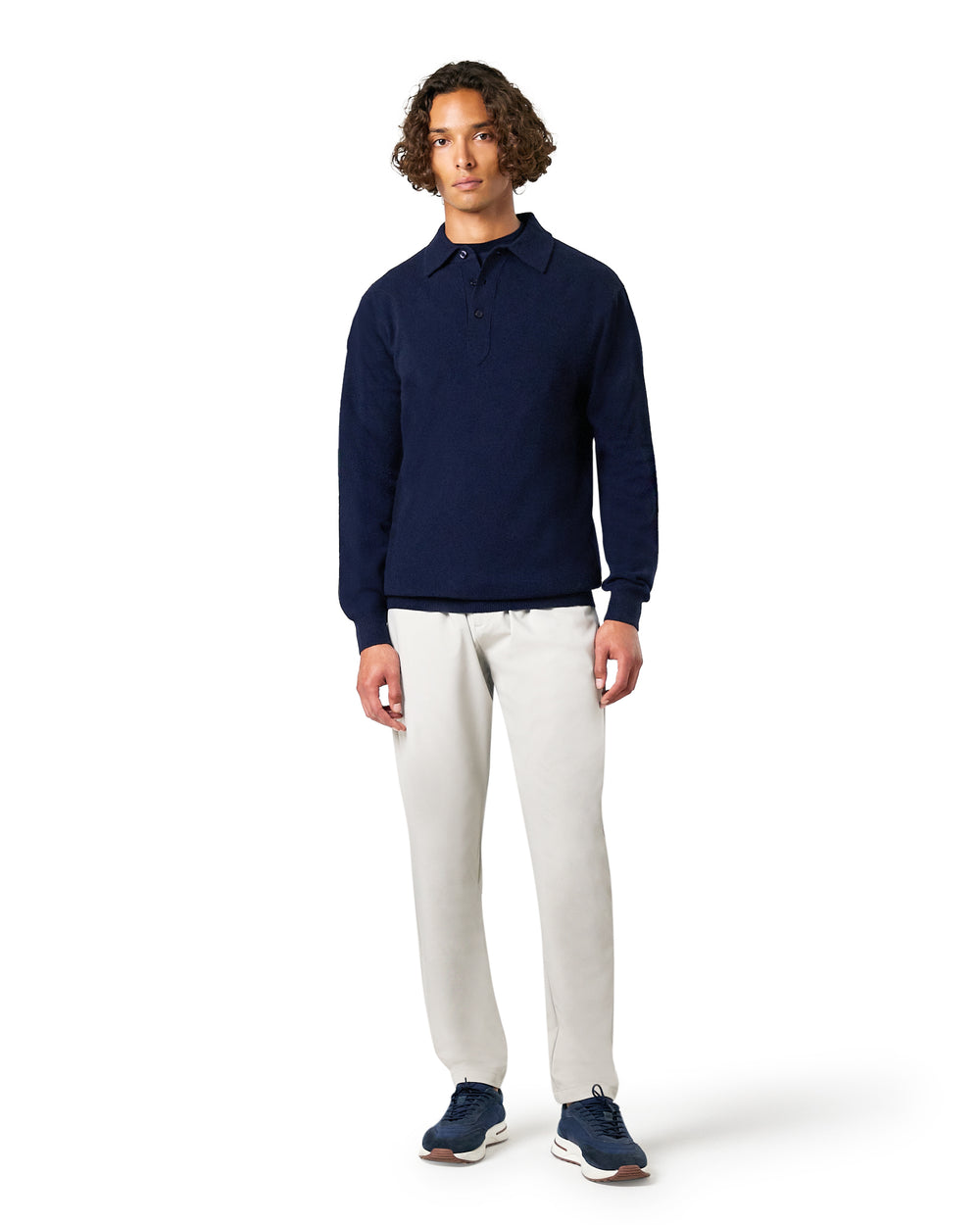 Man wearing a navy long-sleeve polo shirt and white pants on a white background