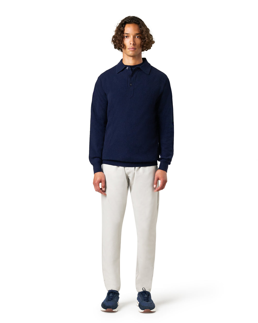 Man wearing a navy sweater and white pants on a white background
