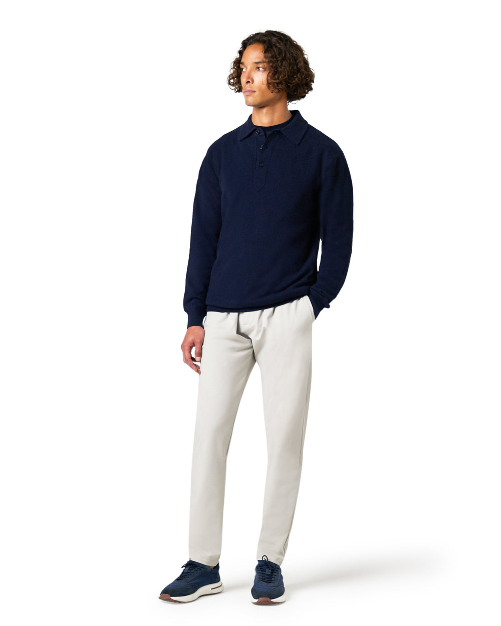 Man wearing a navy sweater and white pants on a white background
