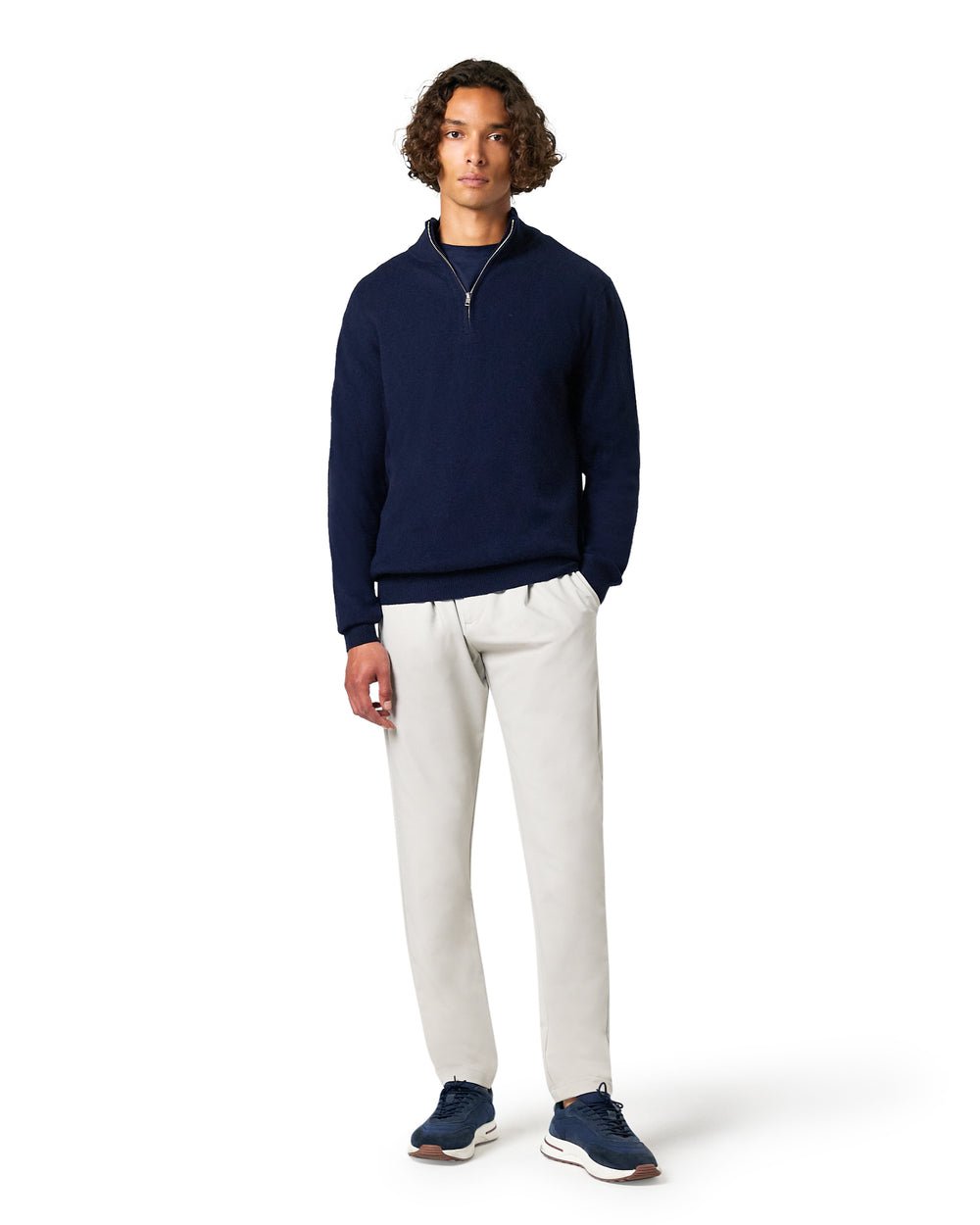 Man wearing a navy sweater and white pants on a white background