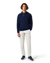 Man wearing a navy sweater and white pants on a white background