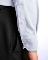 Close-up of a light blue shirt with rolled-up sleeves and dark pants on a white background