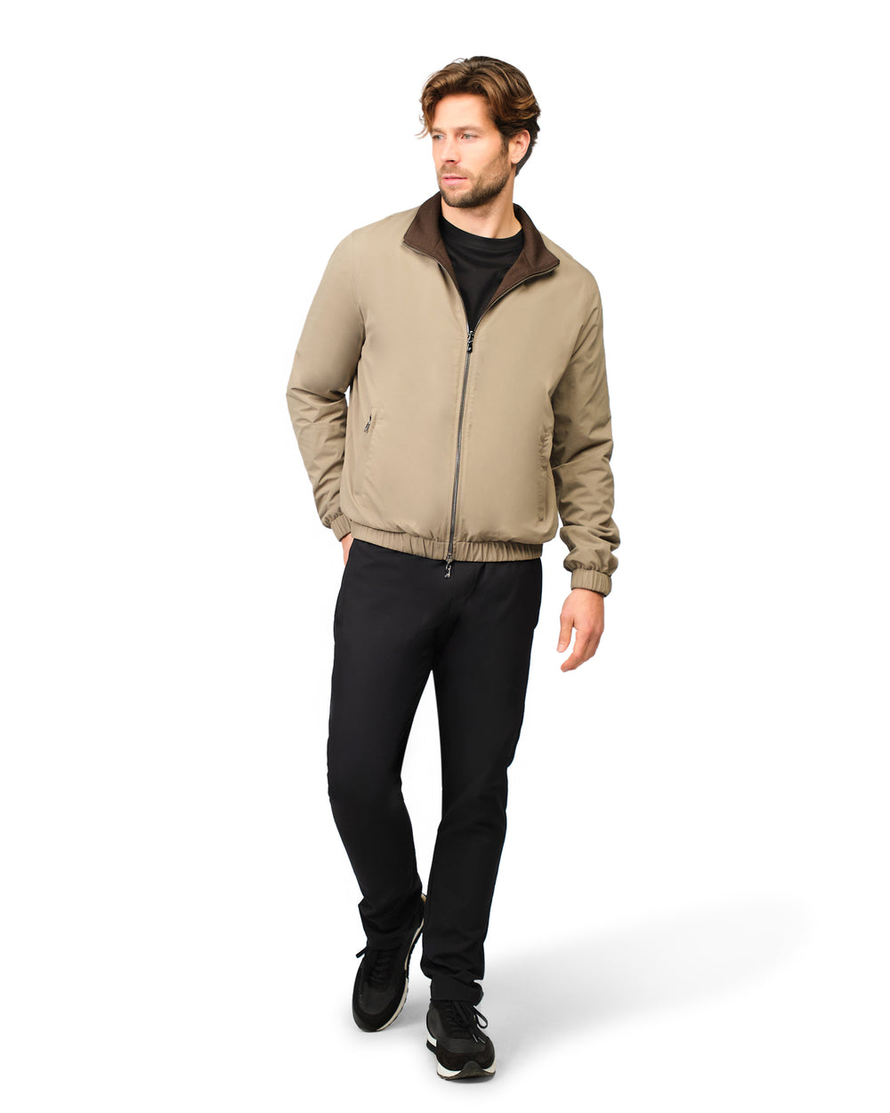 Man wearing a beige jacket with a dark collar and black pants on a white background