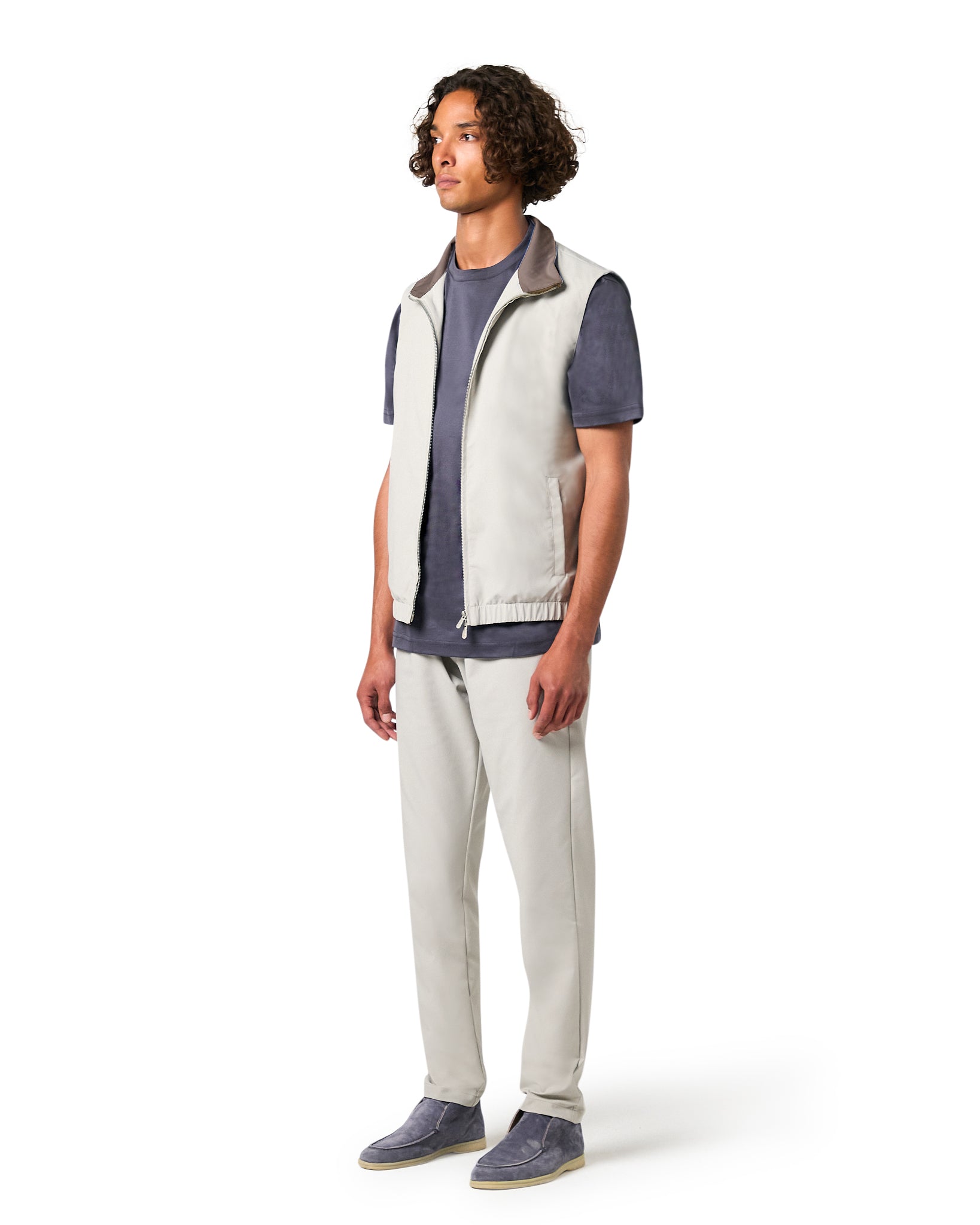 Man wearing a white vest over a blue shirt with gray pants on a white background