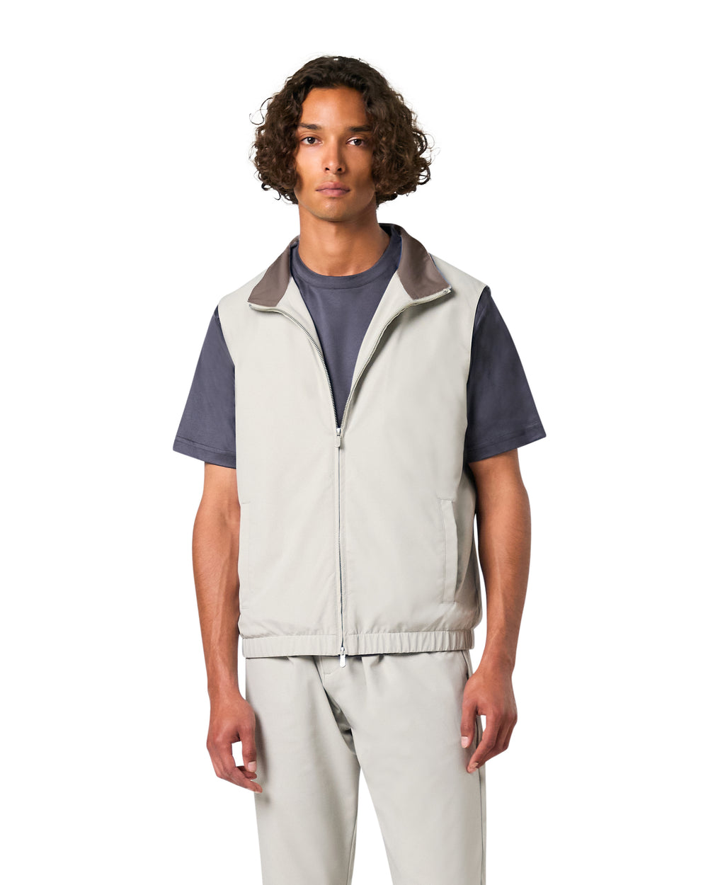 Man wearing a light gray vest over a dark shirt on a white background
