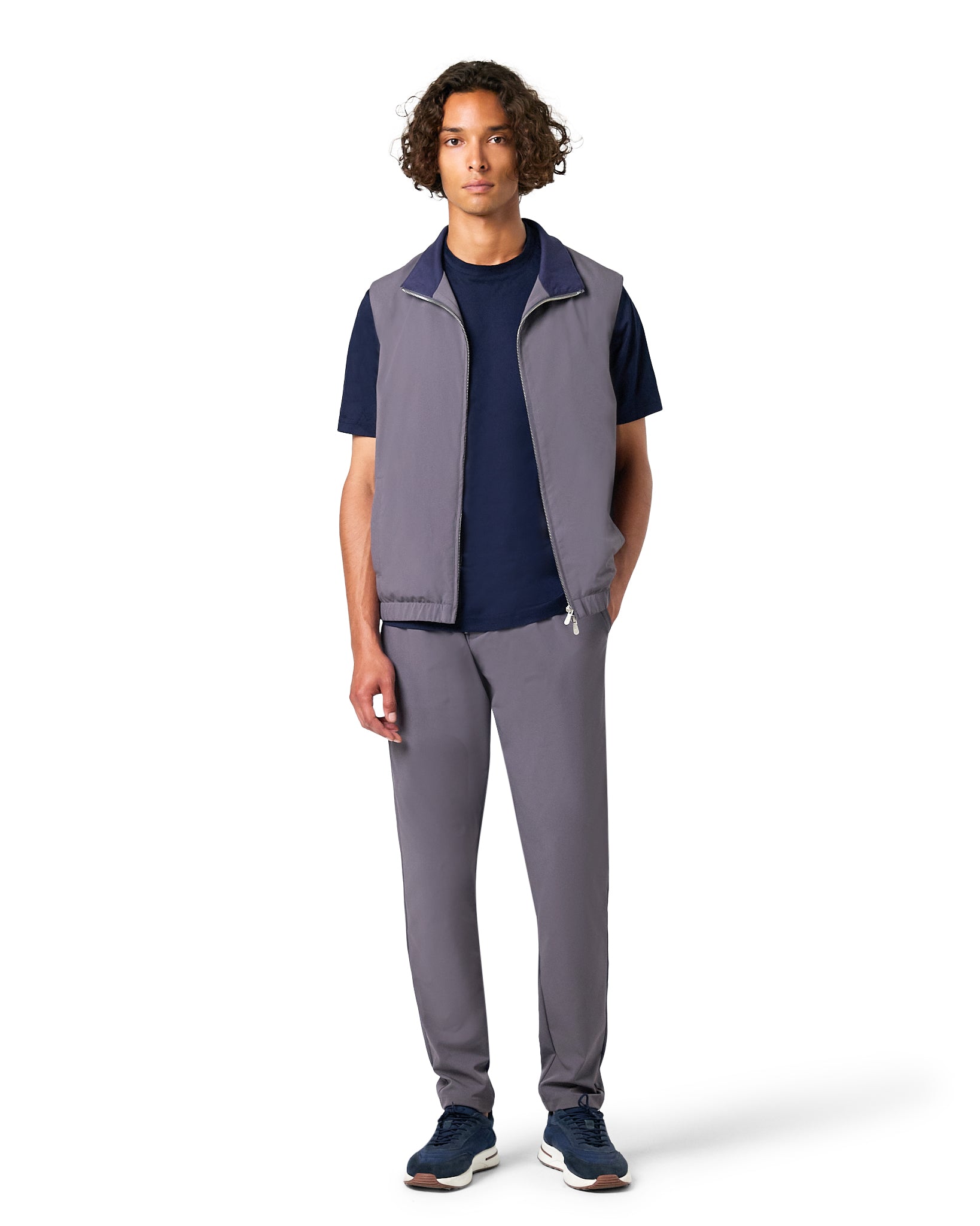 Man wearing a gray vest over a navy shirt with gray pants on a white background