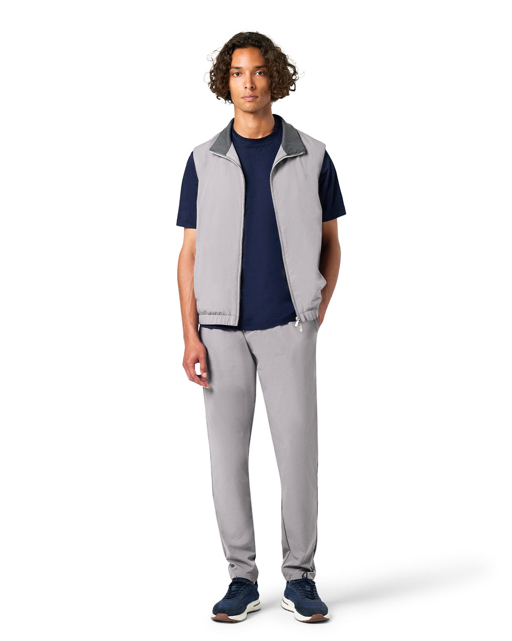 Man wearing a gray vest over a navy shirt with gray pants on a white background