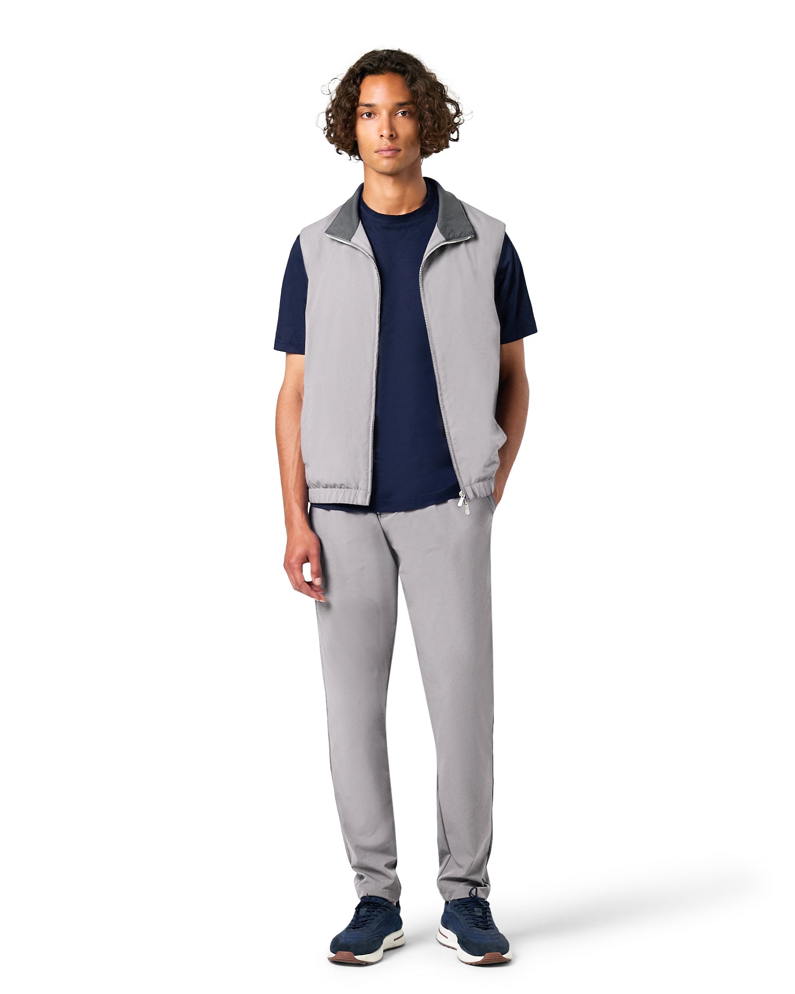 Man wearing a gray vest over a navy shirt with gray pants on a white background