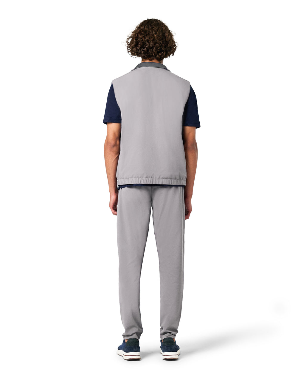 Person wearing a gray vest over a dark shirt with gray pants on a white background
