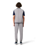 Person wearing a gray vest over a dark shirt with gray pants on a white background