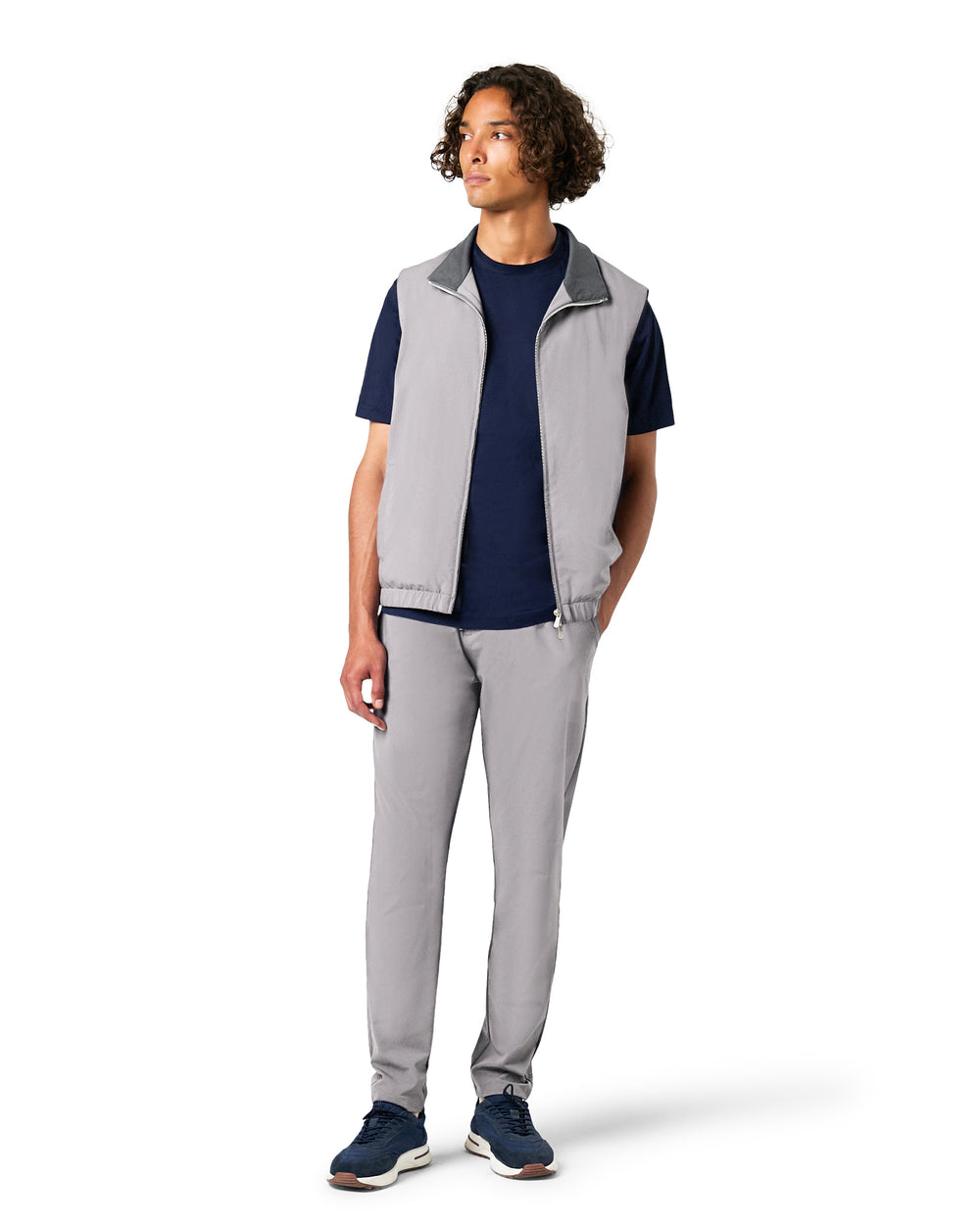 Person wearing a gray vest over a navy shirt with gray pants on a white background